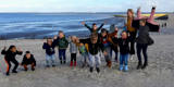 Kinderen en begeleiders springen in de lucht op het strand.